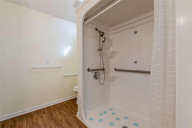 bathroom featuring baseboards, toilet, walk in shower, and wood finished floors