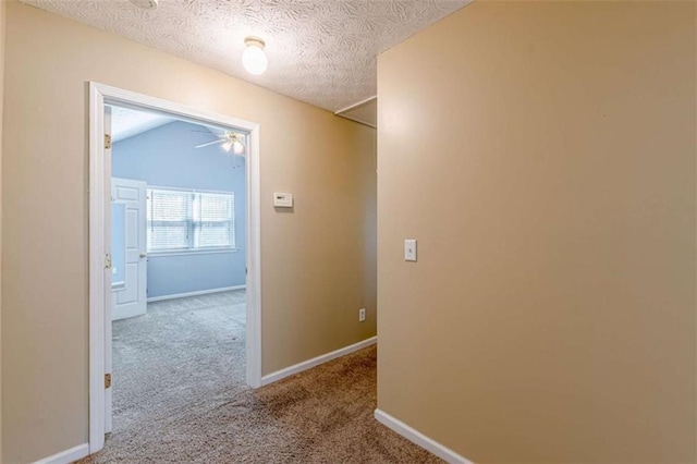 corridor with vaulted ceiling, carpet flooring, baseboards, and a textured ceiling