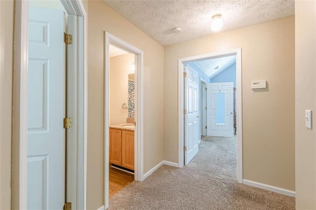 hall with a textured ceiling, vaulted ceiling, baseboards, and light carpet