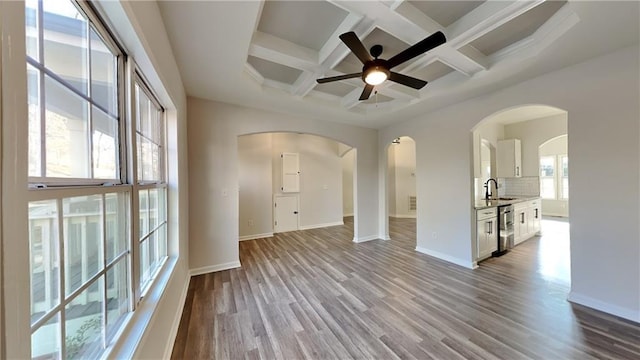 unfurnished living room with light hardwood / wood-style floors, coffered ceiling, ceiling fan, beamed ceiling, and sink