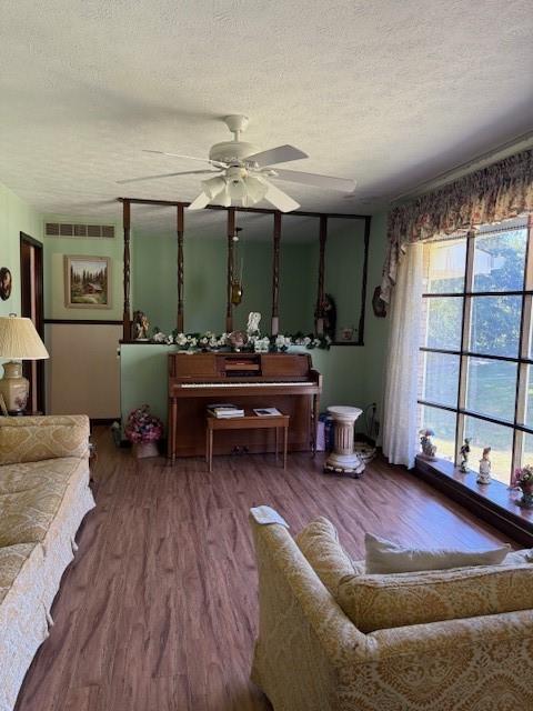 living area featuring a textured ceiling, a ceiling fan, visible vents, and wood finished floors