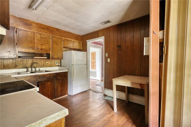 kitchen featuring range, sink, dark wood-type flooring, white refrigerator, and wood walls