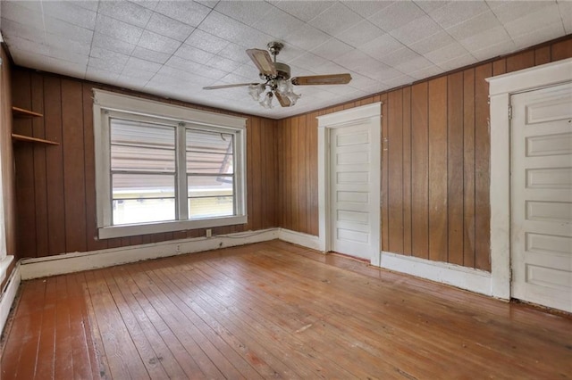 unfurnished room with wood walls, ceiling fan, and light wood-type flooring