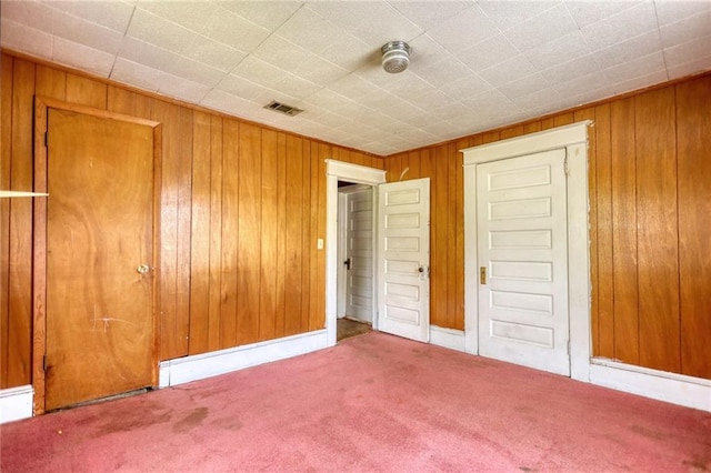 unfurnished bedroom with a closet, wood walls, and carpet floors