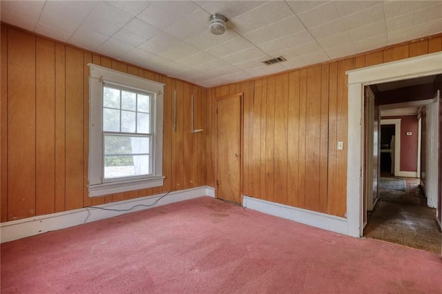 unfurnished room with wood walls and dark colored carpet