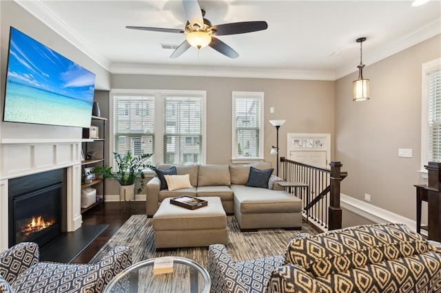 living area with crown molding, visible vents, a glass covered fireplace, wood finished floors, and baseboards