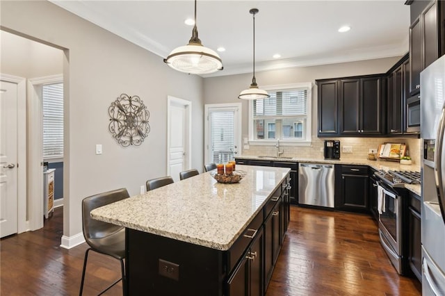 kitchen featuring dark wood finished floors, a kitchen breakfast bar, a sink, stainless steel appliances, and backsplash