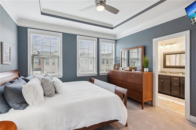 bedroom featuring light carpet, a sink, a raised ceiling, ensuite bath, and crown molding