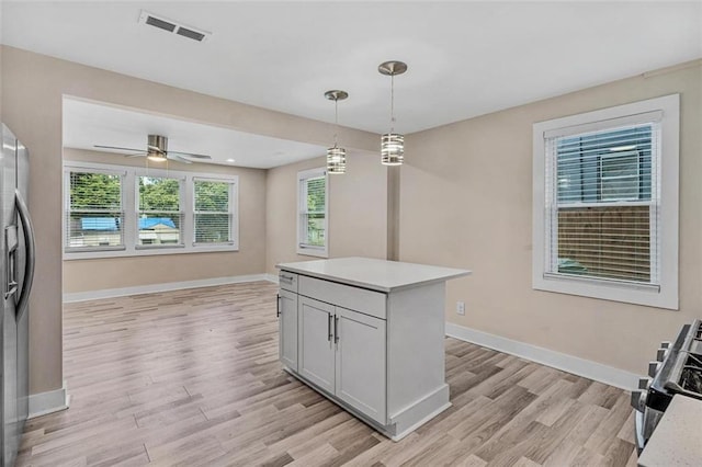 kitchen with pendant lighting, light countertops, visible vents, light wood-type flooring, and baseboards