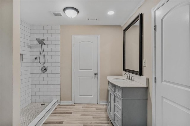 bathroom with a tile shower, wood finished floors, vanity, and visible vents