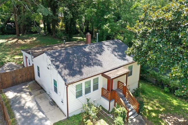 view of front of house featuring roof with shingles, fence, a chimney, and a front lawn