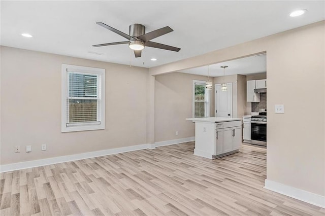 kitchen with white cabinets, a kitchen island, stainless steel gas range, light countertops, and pendant lighting