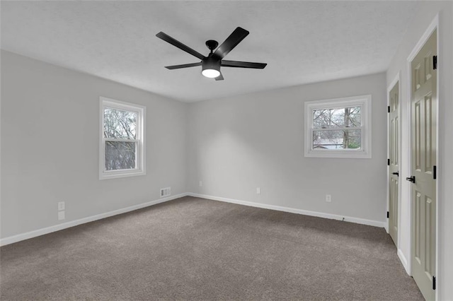 empty room featuring a healthy amount of sunlight, baseboards, dark carpet, and ceiling fan