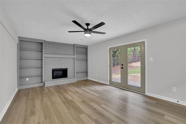 unfurnished living room with light wood-type flooring, built in features, french doors, a fireplace, and baseboards