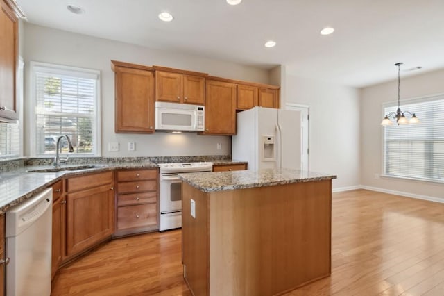 kitchen with a center island, a sink, white appliances, brown cabinets, and light wood-style flooring