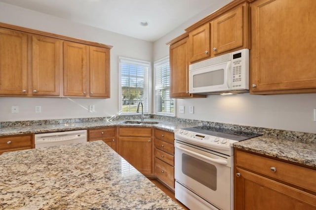 kitchen with brown cabinetry, white appliances, a sink, and light stone counters