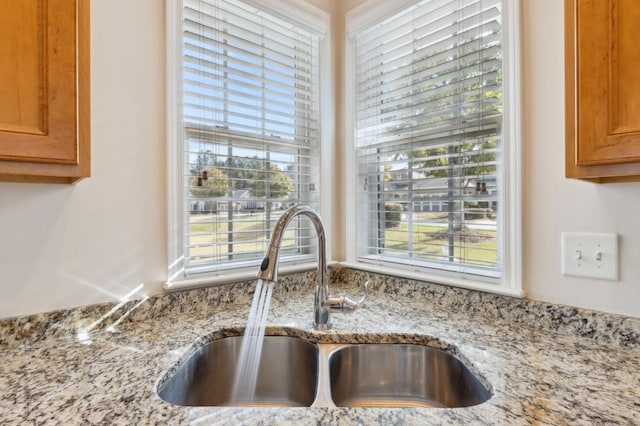 details featuring brown cabinetry, light stone counters, and a sink