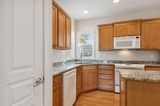 kitchen with light stone countertops, a sink, white appliances, and light wood-type flooring
