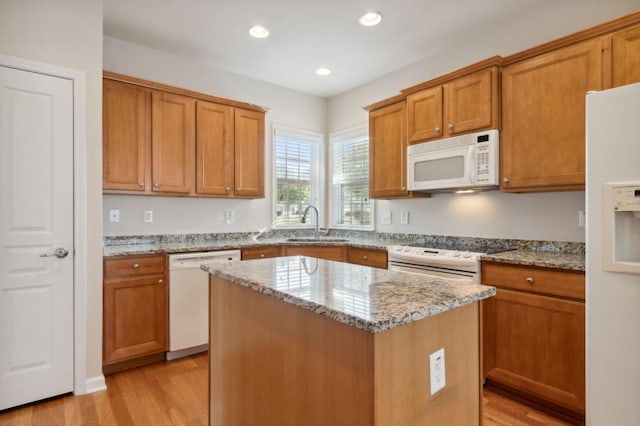 kitchen featuring white appliances, light stone countertops, a center island, a sink, and light wood finished floors