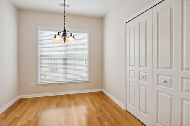 unfurnished dining area featuring light wood-style floors, visible vents, baseboards, and a notable chandelier