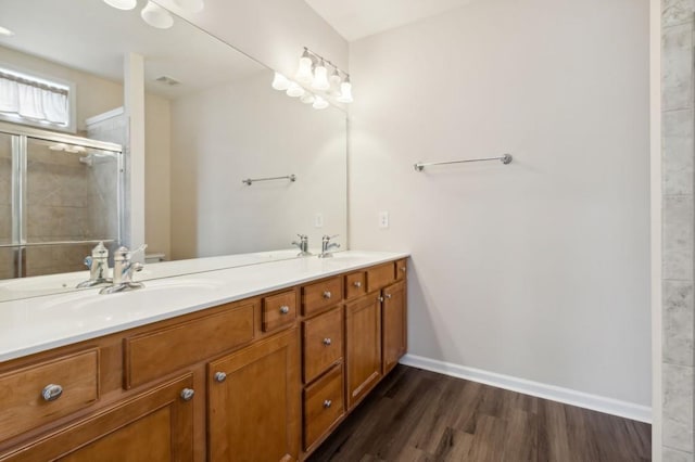 bathroom featuring a sink, a shower stall, double vanity, and wood finished floors