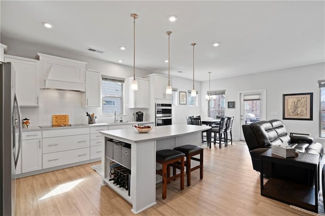 kitchen featuring a breakfast bar, a sink, visible vents, appliances with stainless steel finishes, and custom range hood