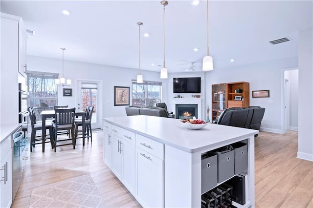 kitchen featuring plenty of natural light, a center island, a lit fireplace, light countertops, and light wood-type flooring