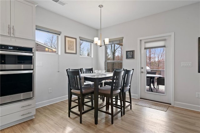 dining space with a chandelier, baseboards, visible vents, and light wood finished floors