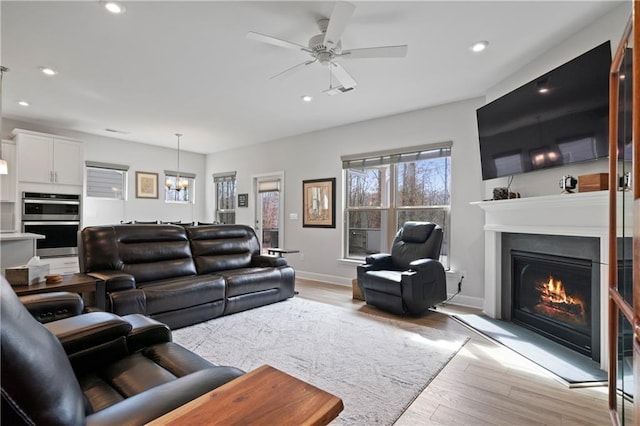 living room with a warm lit fireplace, baseboards, light wood finished floors, and recessed lighting