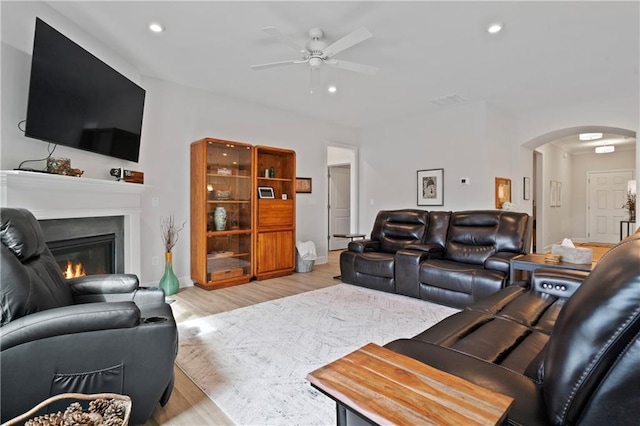 living room featuring light wood finished floors, arched walkways, a glass covered fireplace, ceiling fan, and recessed lighting