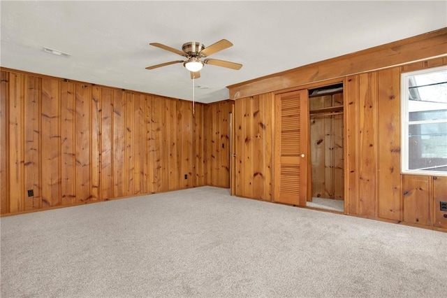 spare room with wooden walls, visible vents, carpet flooring, and a ceiling fan