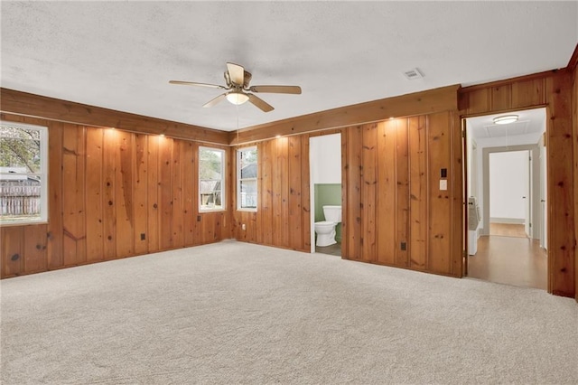 carpeted spare room with a ceiling fan, visible vents, attic access, wood walls, and a textured ceiling