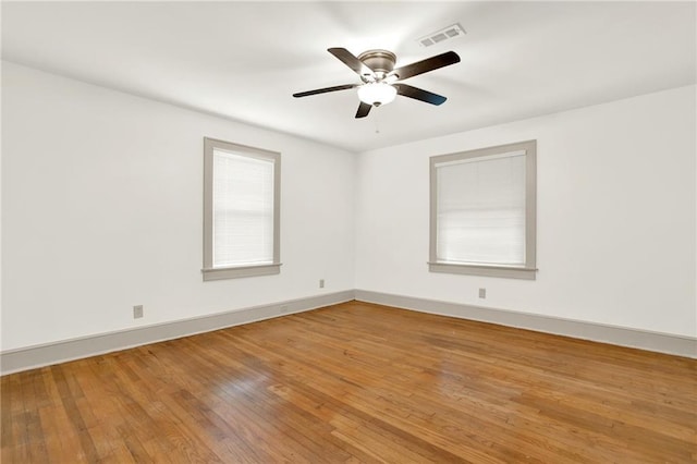 unfurnished room featuring hardwood / wood-style flooring, a ceiling fan, baseboards, and visible vents