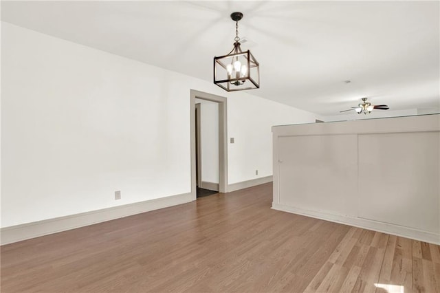 unfurnished room featuring ceiling fan with notable chandelier, wood finished floors, and baseboards