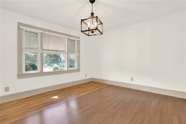 unfurnished room with baseboards, wood finished floors, and a chandelier