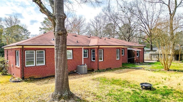 back of house with fence, central AC, a fire pit, a lawn, and brick siding