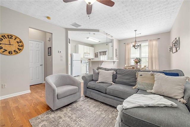 living room with ceiling fan with notable chandelier, light hardwood / wood-style flooring, and a textured ceiling