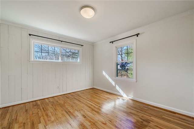 spare room featuring ornamental molding, a wealth of natural light, and light hardwood / wood-style flooring