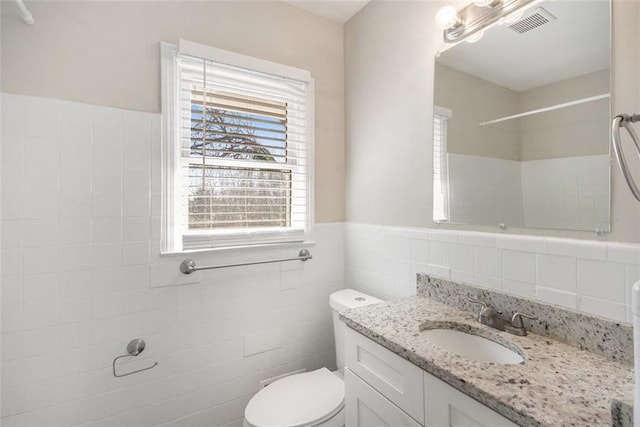 bathroom with vanity, a shower, toilet, and tile walls