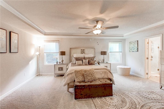 bedroom featuring a raised ceiling, light colored carpet, ensuite bathroom, and ceiling fan