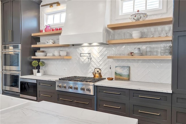 kitchen with light stone countertops, custom range hood, backsplash, and appliances with stainless steel finishes