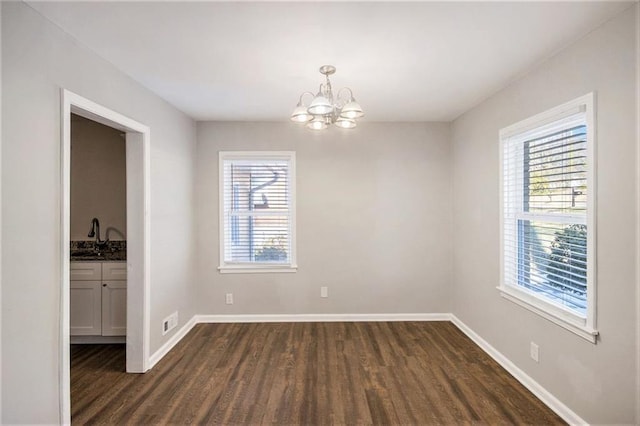 spare room featuring a healthy amount of sunlight, dark wood-type flooring, sink, and a chandelier