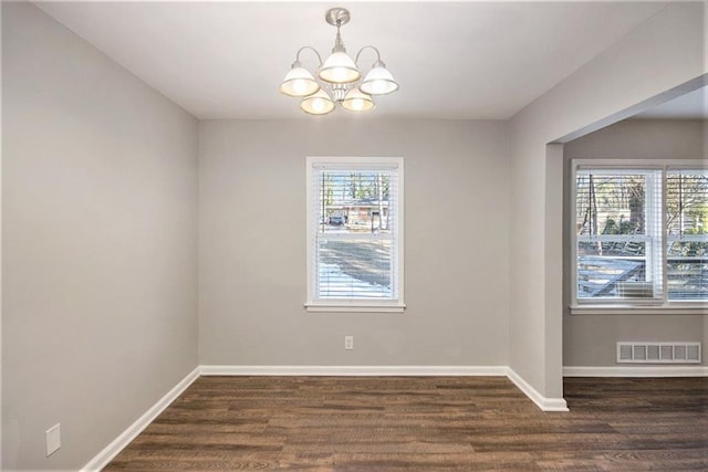 unfurnished room with dark hardwood / wood-style flooring, an inviting chandelier, and plenty of natural light