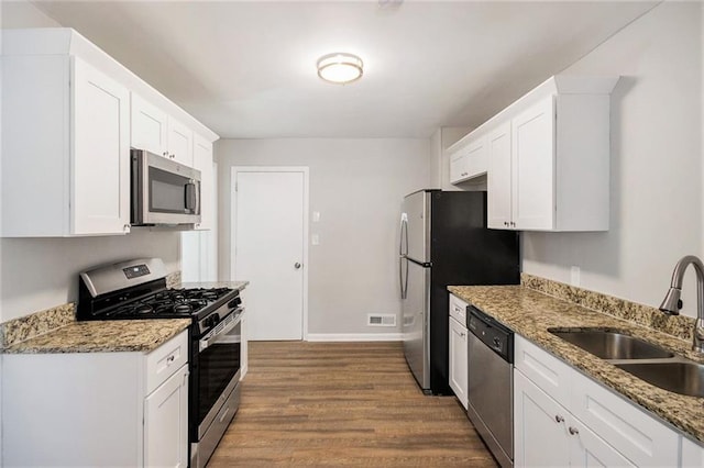 kitchen with appliances with stainless steel finishes, light wood-type flooring, dark stone counters, white cabinets, and sink