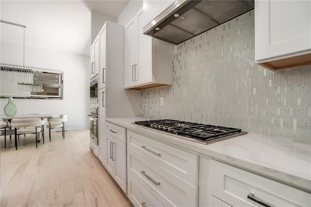 kitchen with light hardwood / wood-style flooring, white cabinets, backsplash, premium range hood, and stainless steel appliances