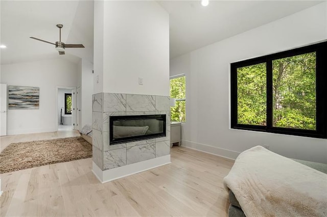 bedroom with light hardwood / wood-style floors, a tiled fireplace, multiple windows, and ceiling fan