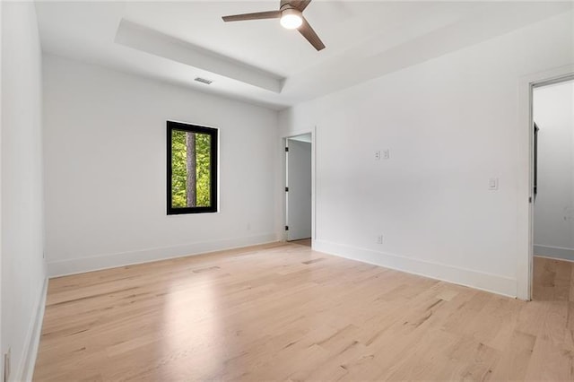 empty room featuring ceiling fan, light wood-type flooring, and a tray ceiling