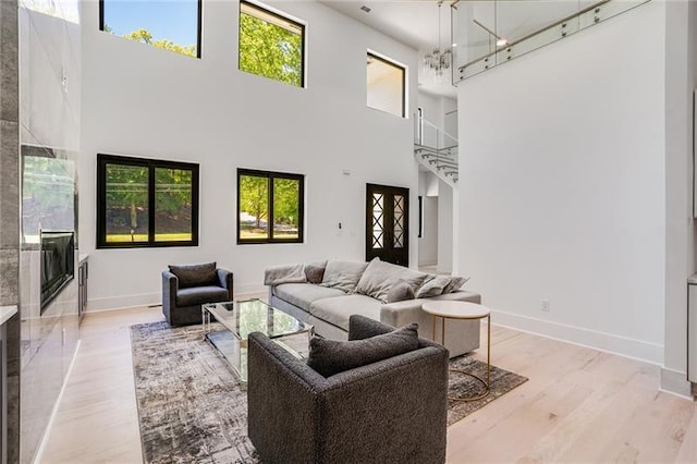 living room with a healthy amount of sunlight, a chandelier, light hardwood / wood-style floors, and a towering ceiling