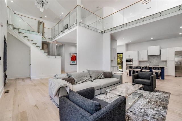 living room with sink, a notable chandelier, light hardwood / wood-style floors, and a towering ceiling