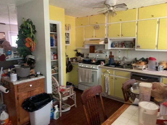kitchen with under cabinet range hood, white range with gas cooktop, yellow cabinets, a sink, and a ceiling fan